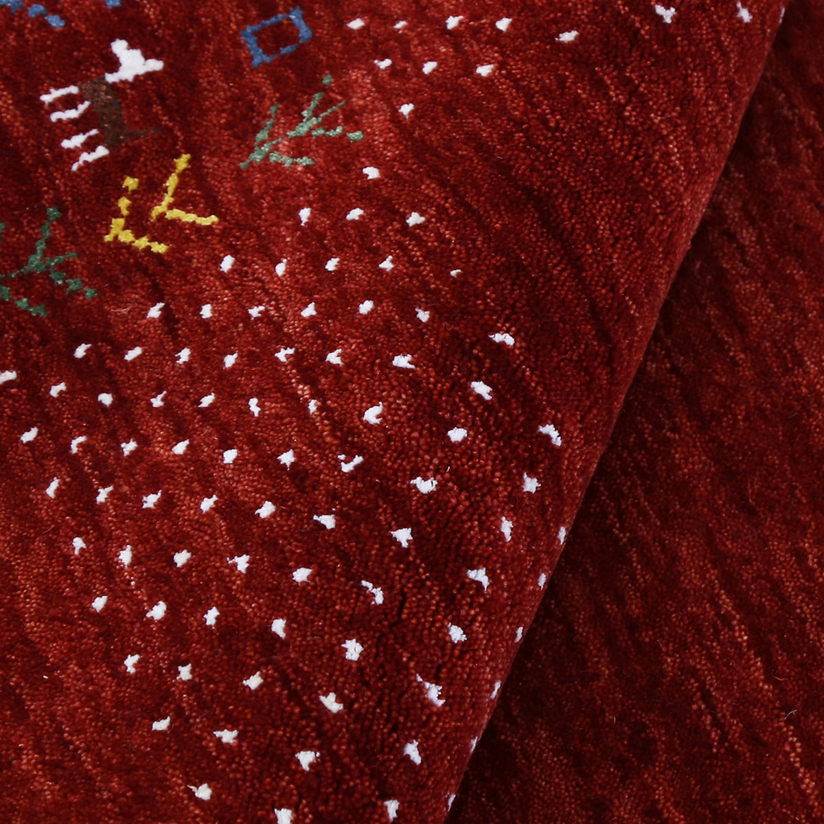 Corner and edge detail of crimson red Loom Lori wool rug showing ivory dotted sections, tribal motifs and handcrafted finishing