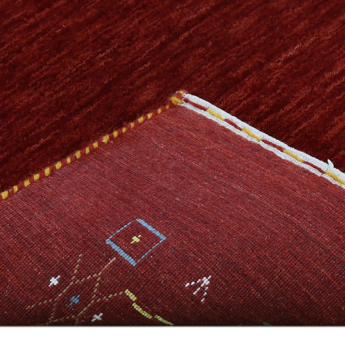 Corner and edge detail of deep red Loom Lori wool rug showing geometric tribal motifs and traditional handcrafted finishing