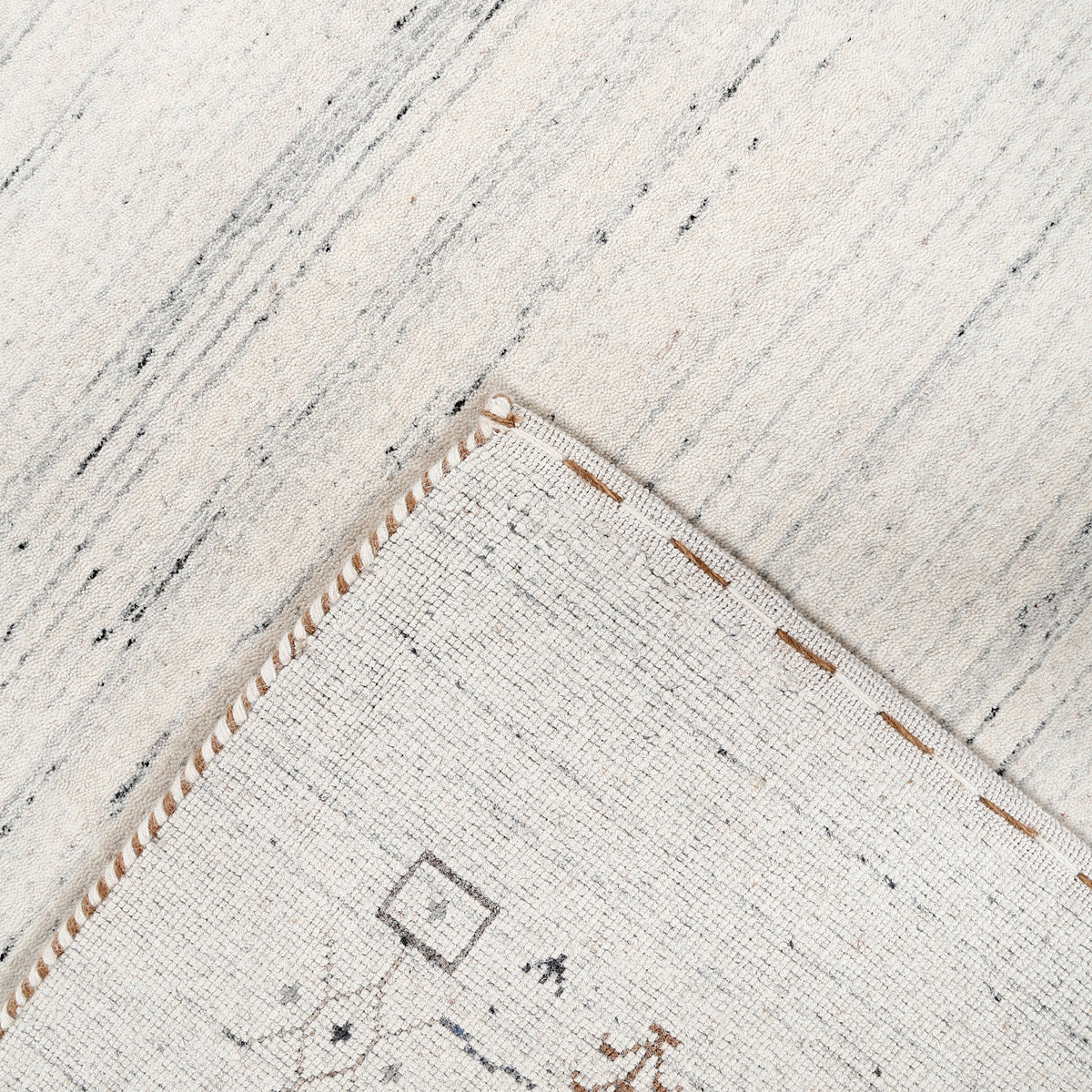 Corner and edge detail of ivory grey Loom Lori wool rug showing symbolic geometric motifs and handcrafted finishing