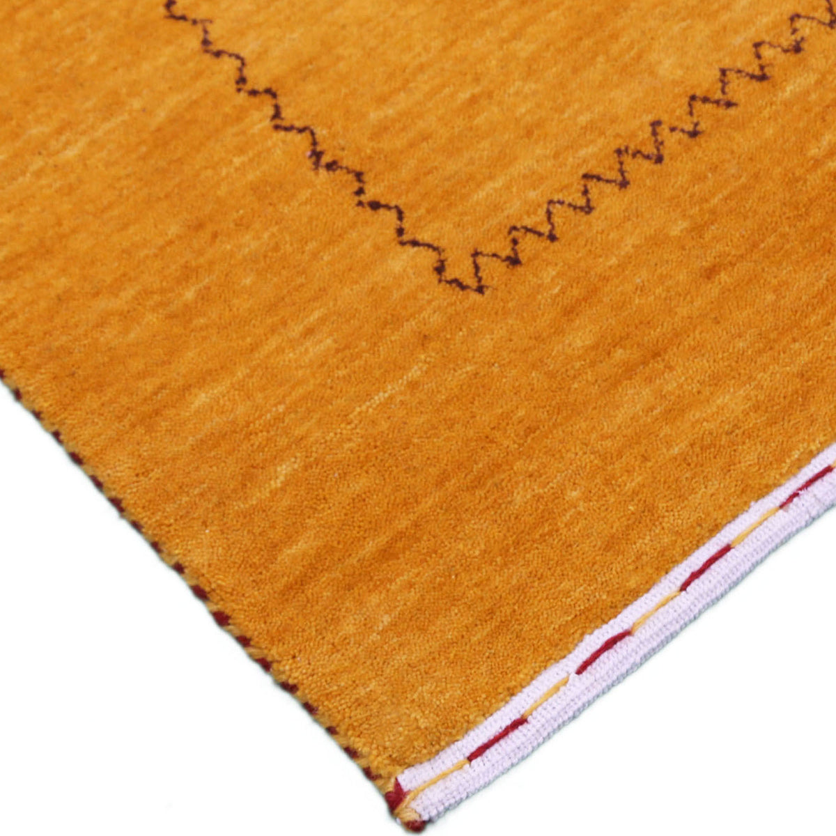 Corner and edge detail of golden mustard Loom Lori wool rug showing dark zigzag border and traditional handcrafted finishing