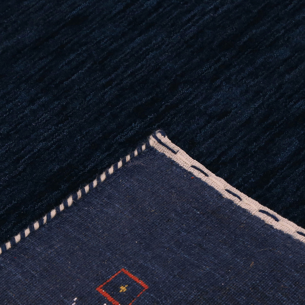 Corner and edge detail of navy blue Loom Lori wool rug showing geometric tribal motifs and handcrafted finishing