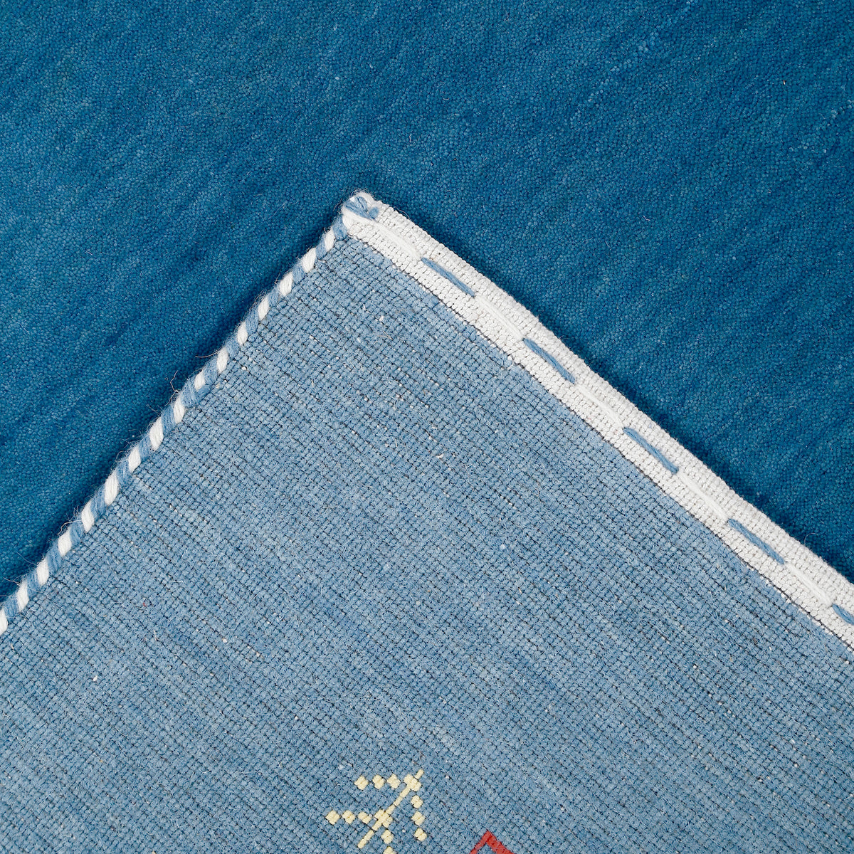 Corner and edge detail of ocean blue Loom Lori wool rug showing ivory dotted sections, symbolic folk motifs and handcrafted finishing