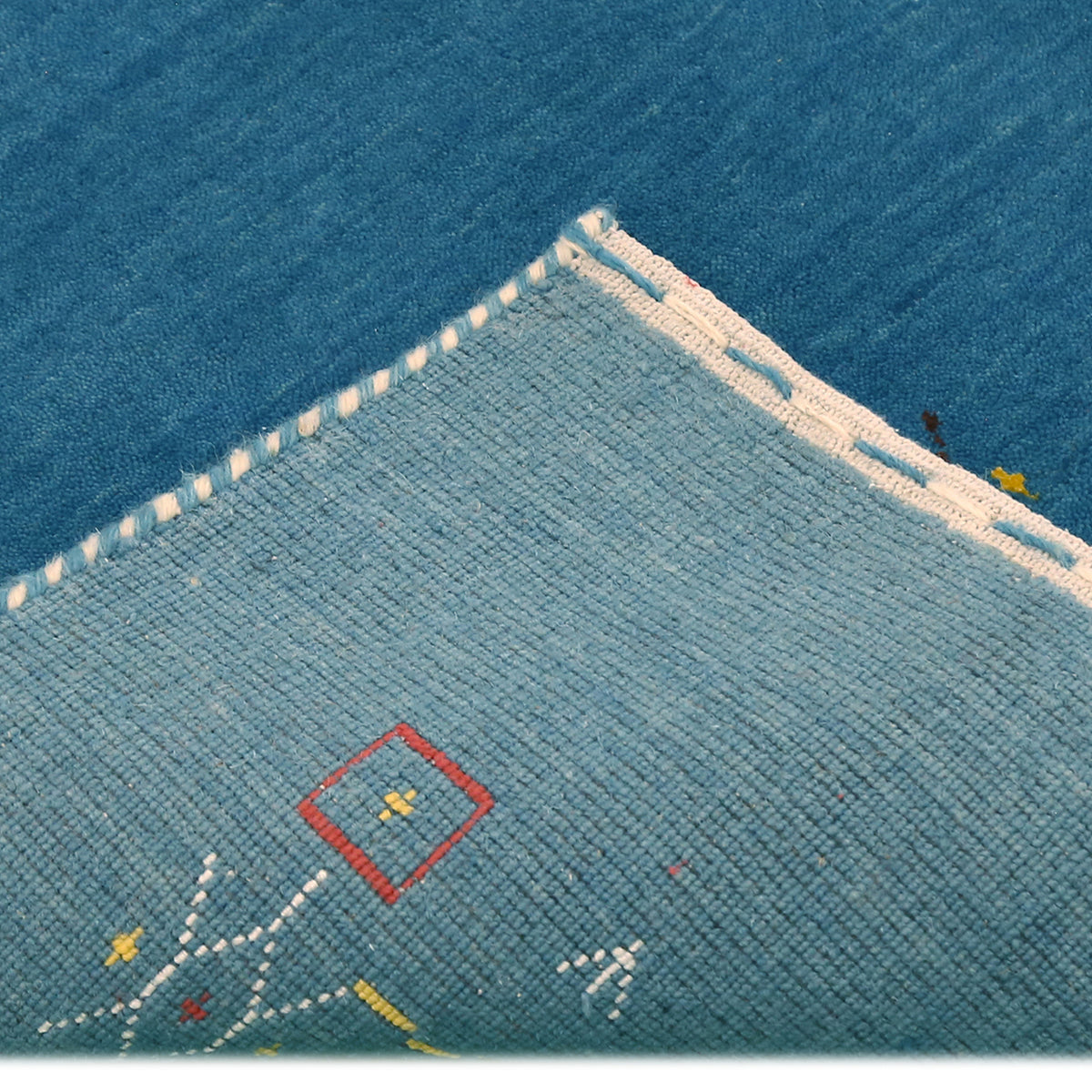 Corner and edge detail of teal blue Loom Lori wool rug showing geometric tribal motifs and traditional handcrafted finishing