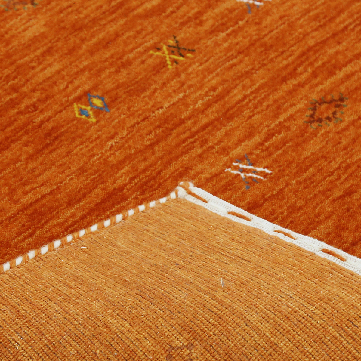 Corner and edge detail of terracotta orange Loom Lori wool rug showing subtle geometric border and handcrafted finishing