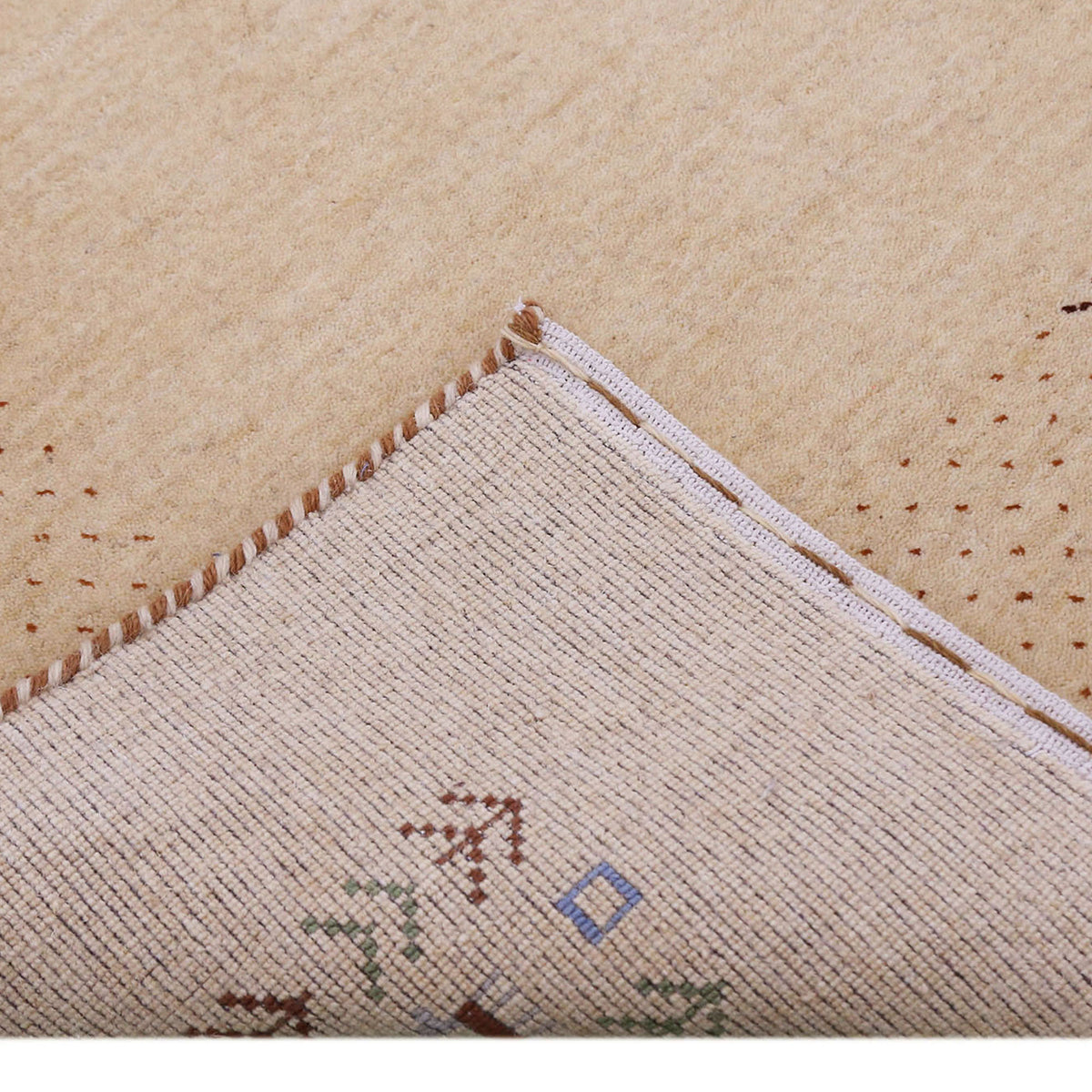 Corner and edge detail of natural beige Loom Lori wool rug showing dotted border, tribal motifs and handcrafted finishing