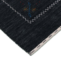 Corner and edge detail of black Hand Woven Loom Lori wool rug showing zigzag geometric border and handcrafted finishing