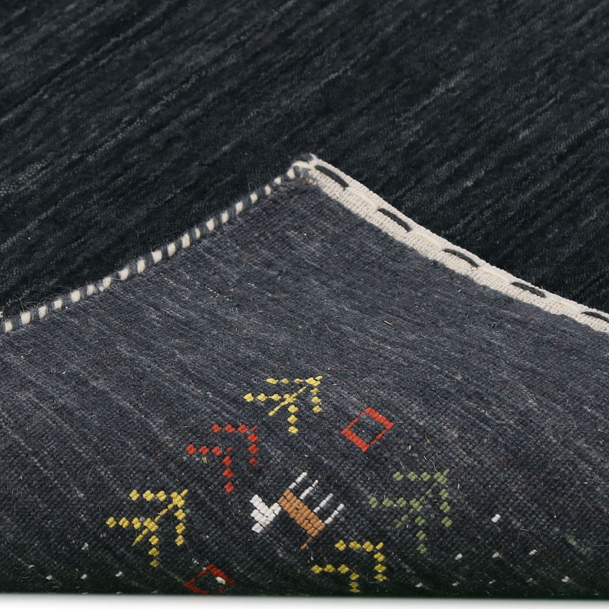 Corner and edge detail of charcoal black Loom Lori wool rug showing ivory dotted sections, folk motifs and handcrafted finishing