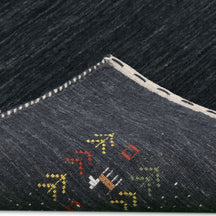 Corner and edge detail of charcoal black Loom Lori wool rug showing ivory dotted sections, folk motifs and handcrafted finishing