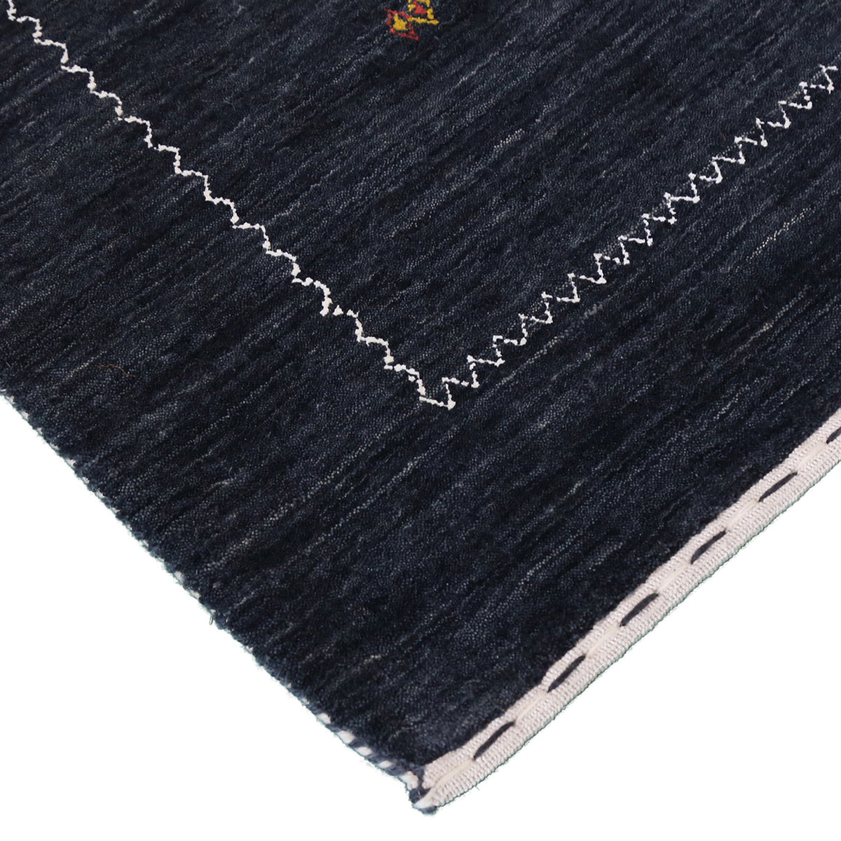 Corner and edge detail of charcoal black Loom Lori wool rug showing contrasting ivory zigzag border and handcrafted finishing