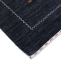 Corner and edge detail of charcoal black Loom Lori wool rug showing contrasting ivory zigzag border and handcrafted finishing