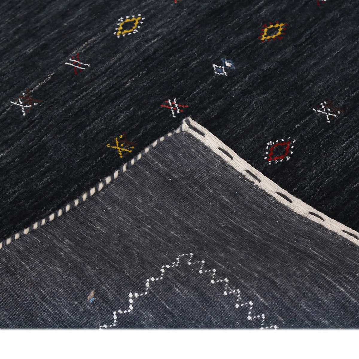 Corner and edge detail of charcoal black Loom Lori wool rug showing contrasting ivory zigzag border and handcrafted finishing