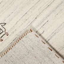 Corner and edge detail of ivory cream Hand Woven Loom Lori wool rug showing grey striations and handcrafted finishing
