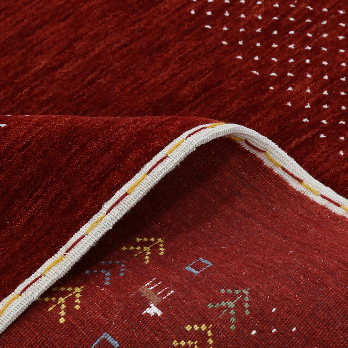 Corner and edge detail of crimson red Loom Lori wool rug showing ivory dotted sections, tribal motifs and handcrafted finishing