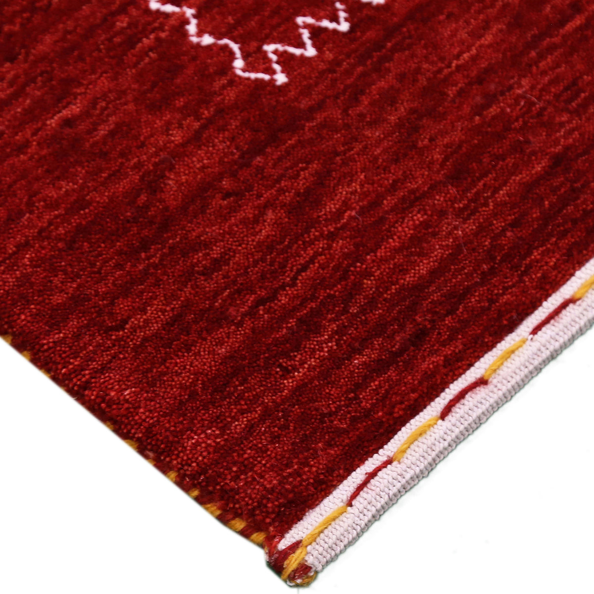 Corner and edge detail of crimson red Loom Lori wool rug showing contrasting ivory zigzag border and handcrafted finishing
