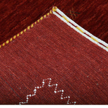 Corner and edge detail of crimson red Loom Lori wool rug showing contrasting ivory zigzag border and handcrafted finishing