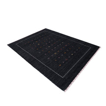 Side perspective of charcoal black Hand Woven Loom Lori wool rug highlighting natural texture, scattered motifs and ivory zigzag border design