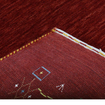Corner and edge detail of deep red Loom Lori wool rug showing geometric tribal motifs and traditional handcrafted finishing