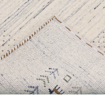 Corner and edge detail of ivory blue-grey Loom Lori wool rug showing dotted border, folk motifs and handcrafted finishing
