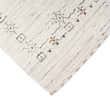 Corner and edge detail of ivory grey Loom Lori wool rug showing symbolic geometric motifs and handcrafted finishing