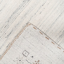 Corner and edge detail of ivory grey Loom Lori wool rug showing symbolic geometric motifs and handcrafted finishing