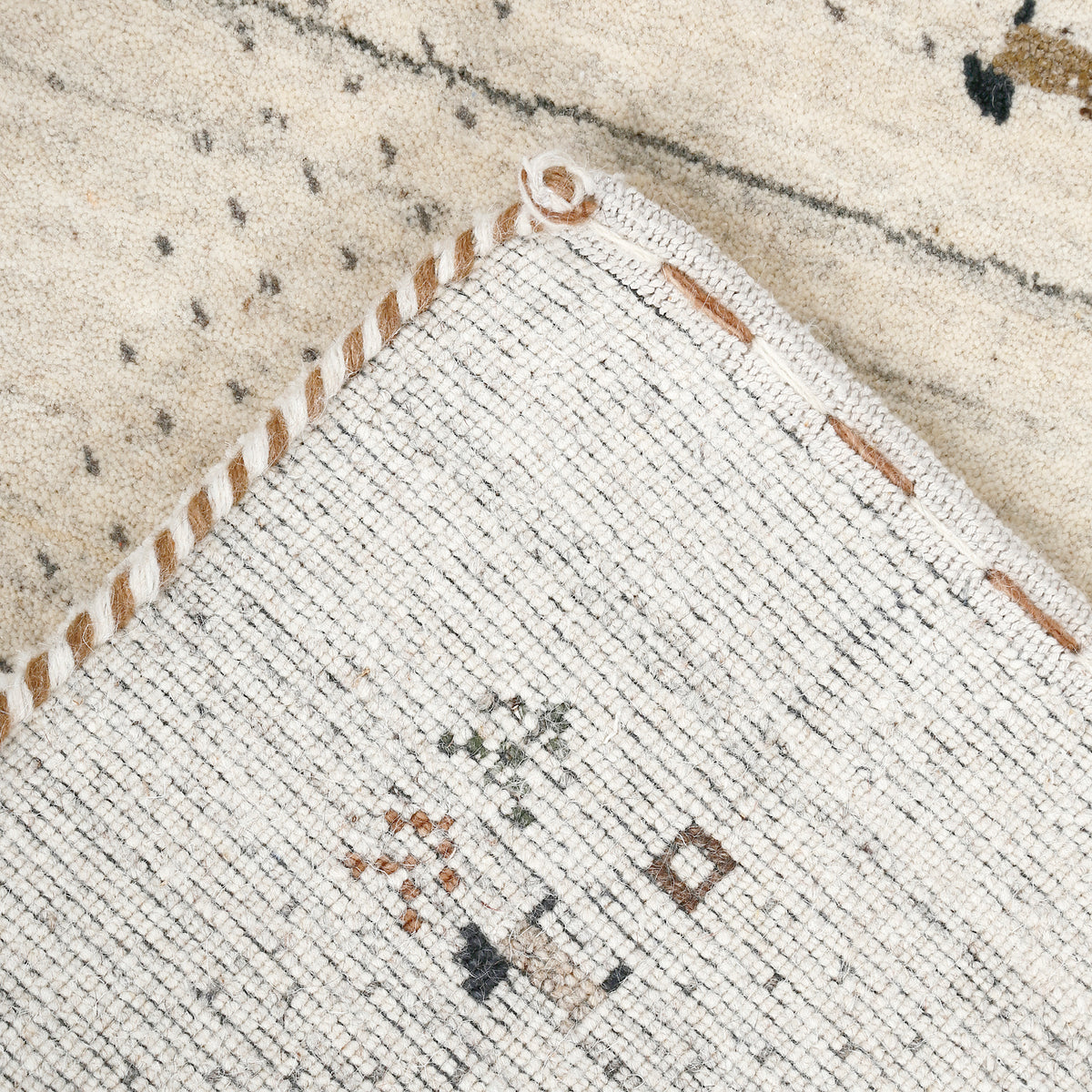Corner and edge detail of ivory Loom Lori wool rug showing dotted border, tree motifs, animal figures and handcrafted finishing