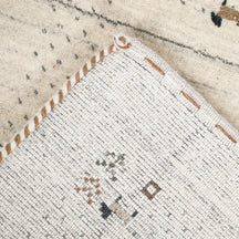 Corner and edge detail of ivory Loom Lori wool rug showing dotted border, tree motifs, animal figures and handcrafted finishing