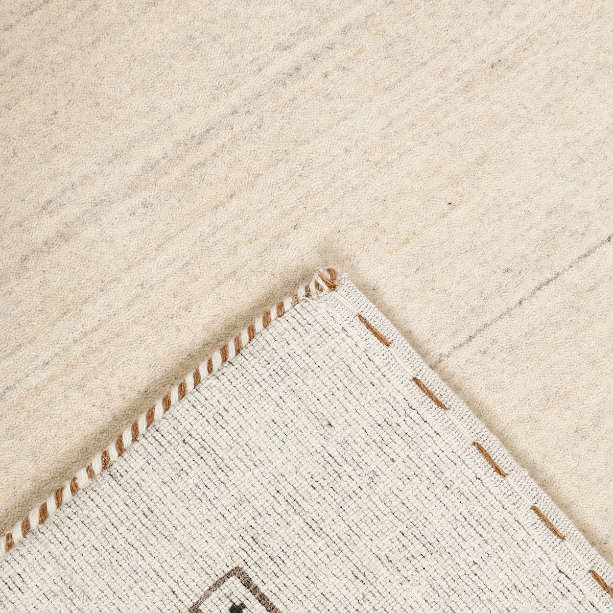 Corner and edge detail of ivory Loom Lori wool rug showing geometric motifs and traditional handcrafted finishing