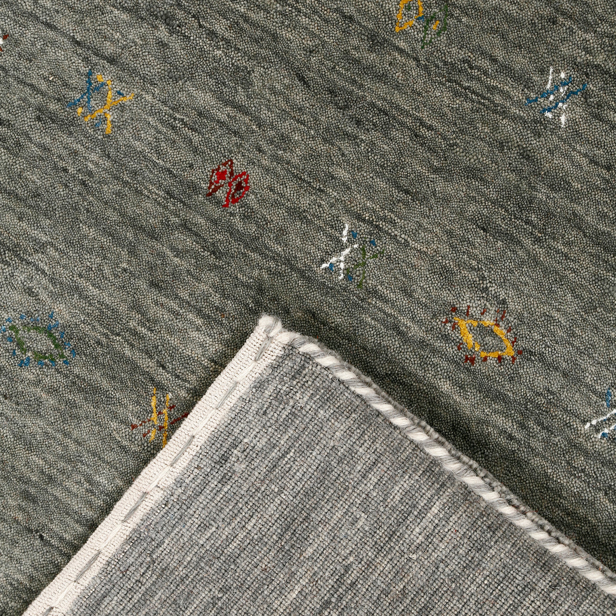 Corner and edge detail of slate grey Loom Lori wool rug showing rust-brown zigzag border and traditional handcrafted finishing