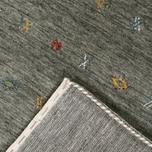 Corner and edge detail of slate grey Loom Lori wool rug showing rust-brown zigzag border and traditional handcrafted finishing