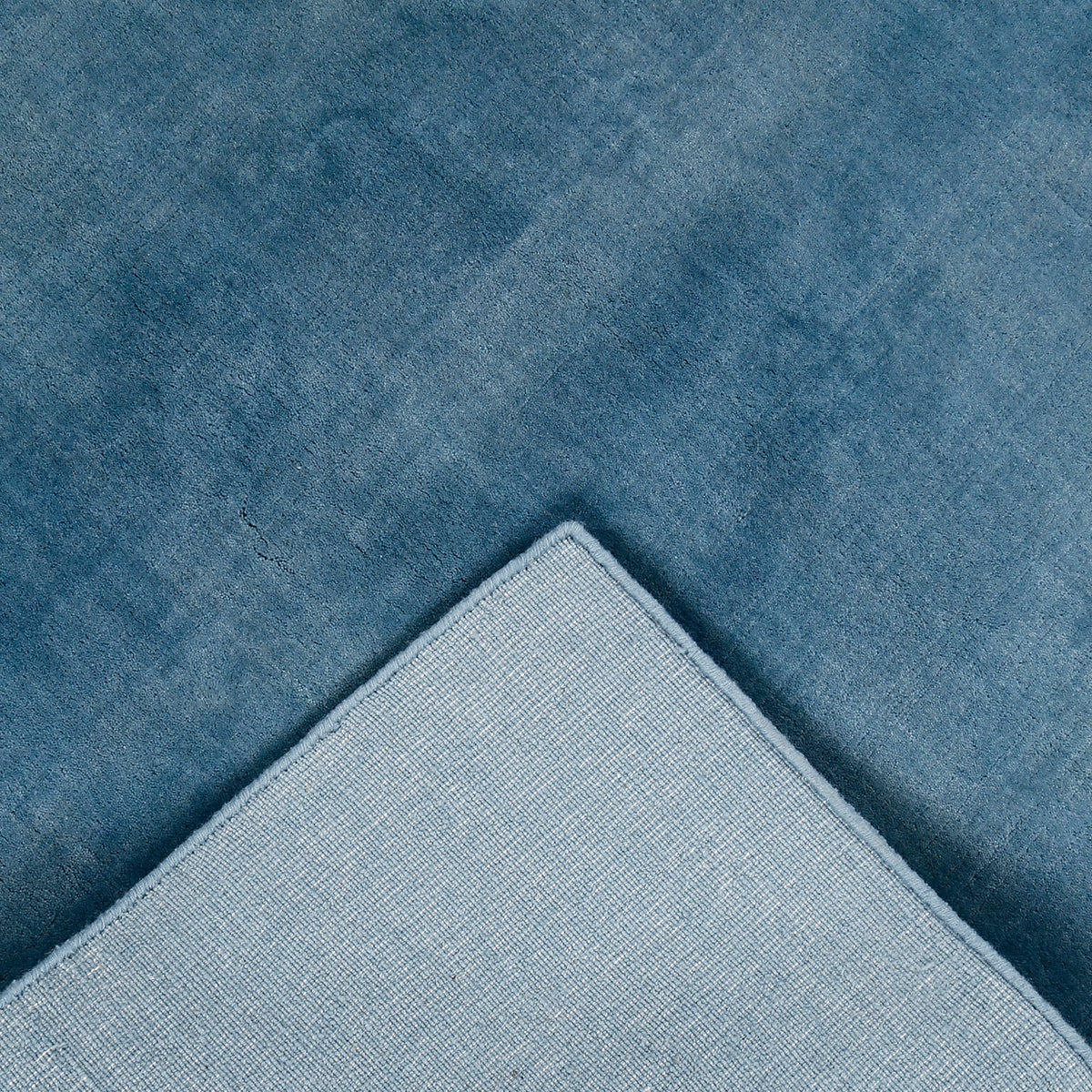 Back and edge detail of light blue hand woven Loom Lori wool rug showing its woven construction, finished border and handcrafted structure.