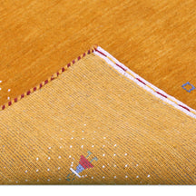 Corner and edge detail of golden mustard Loom Lori wool rug showing ivory dotted sections, folk motifs and handcrafted finishing
