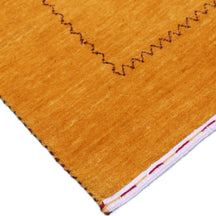 Corner and edge detail of golden mustard Loom Lori wool rug showing dark zigzag border and traditional handcrafted finishing