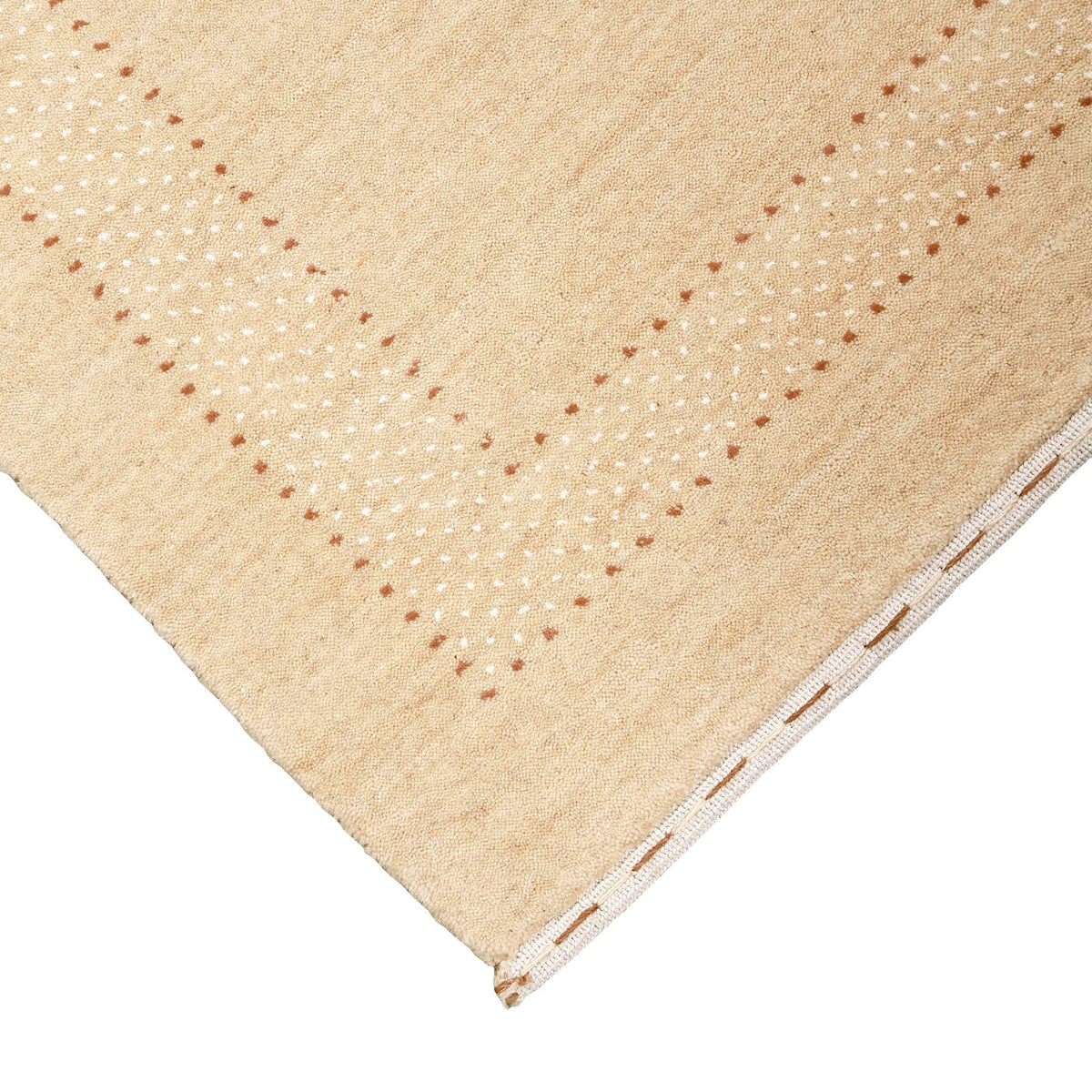 Corner and edge detail of natural beige Loom Lori wool rug showing delicate dotted border and traditional handcrafted finishing