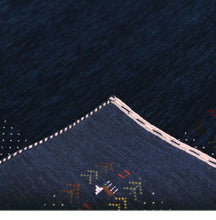 Corner and edge detail of navy blue Loom Lori wool rug showing ivory dotted sections, folk motifs and handcrafted finishing