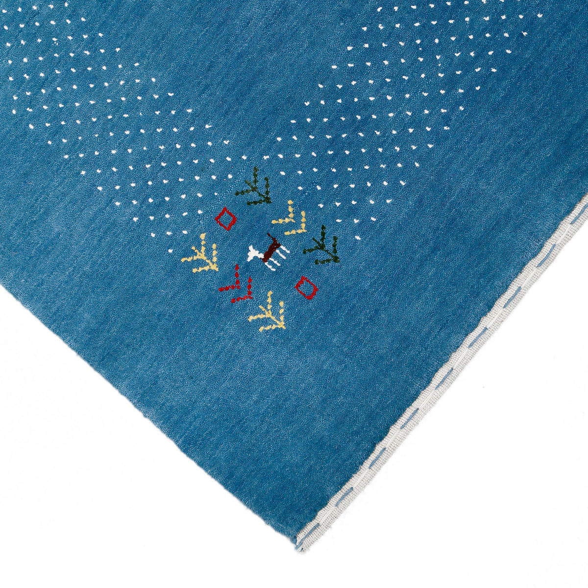 Corner and edge detail of ocean blue Loom Lori wool rug showing ivory dotted sections, symbolic folk motifs and handcrafted finishing