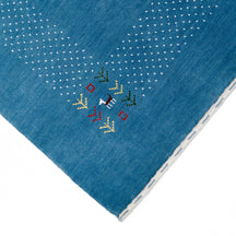 Corner and edge detail of ocean blue Loom Lori wool rug showing ivory dotted sections, symbolic folk motifs and handcrafted finishing