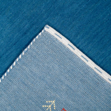 Corner and edge detail of ocean blue Loom Lori wool rug showing ivory dotted sections, symbolic folk motifs and handcrafted finishing