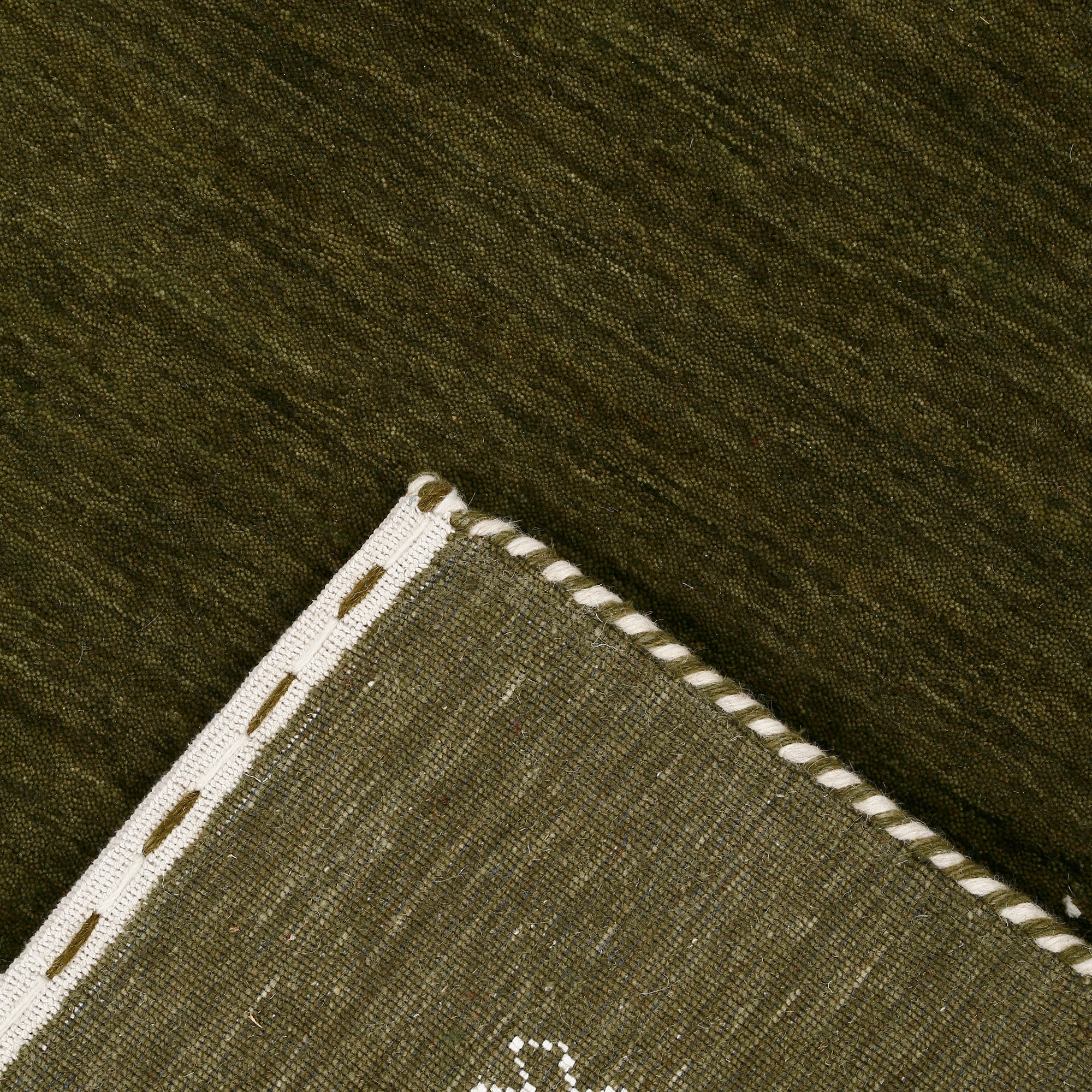 Corner and edge detail of olive green Hand Woven Loom Lori wool rug showing zigzag geometric border and handcrafted finishing