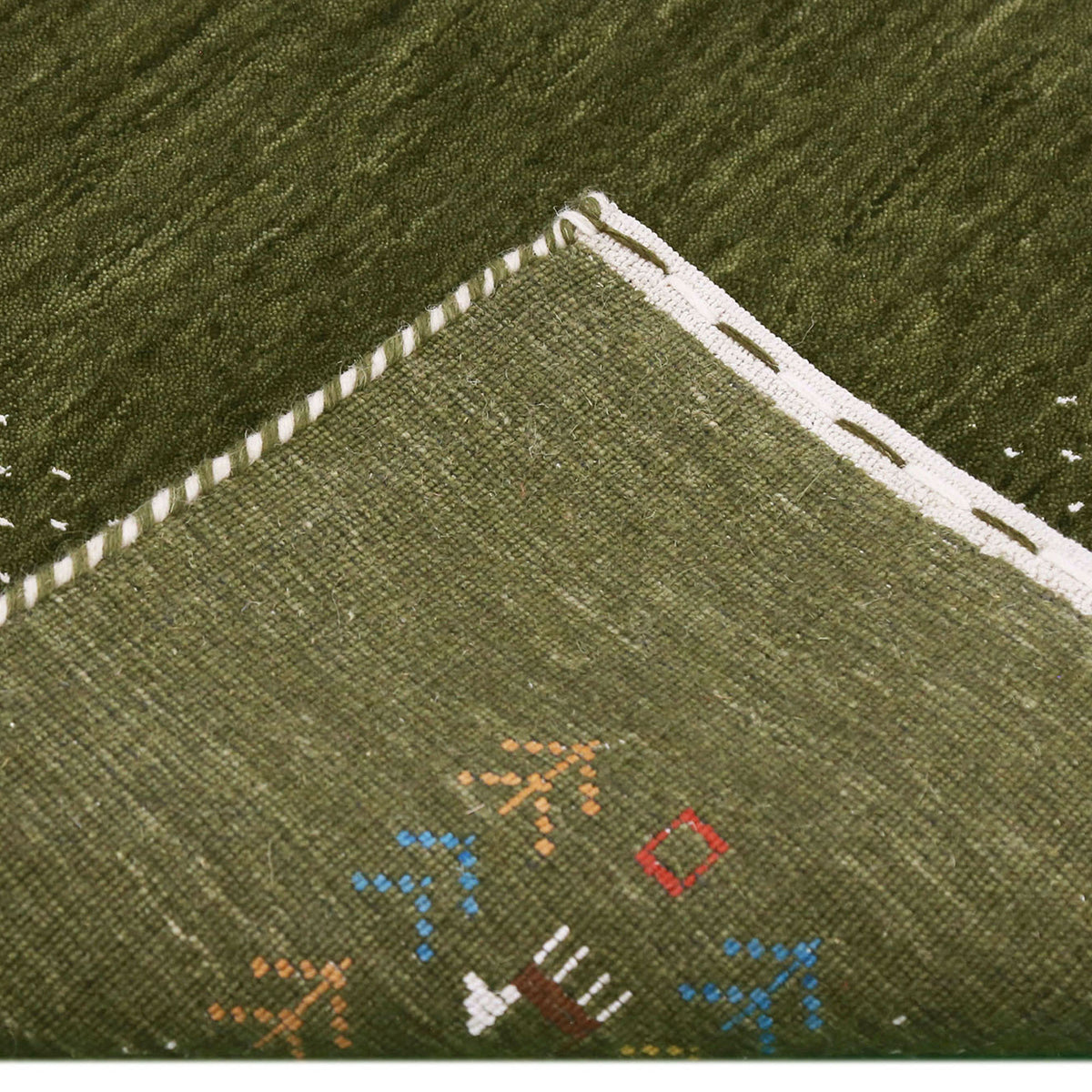 Corner and edge detail of olive green Loom Lori wool rug showing ivory dotted sections, folk motifs and handcrafted finishing