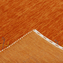 Corner and edge detail of rust orange Hand Woven Loom Lori wool rug showing geometric border and handcrafted finishing