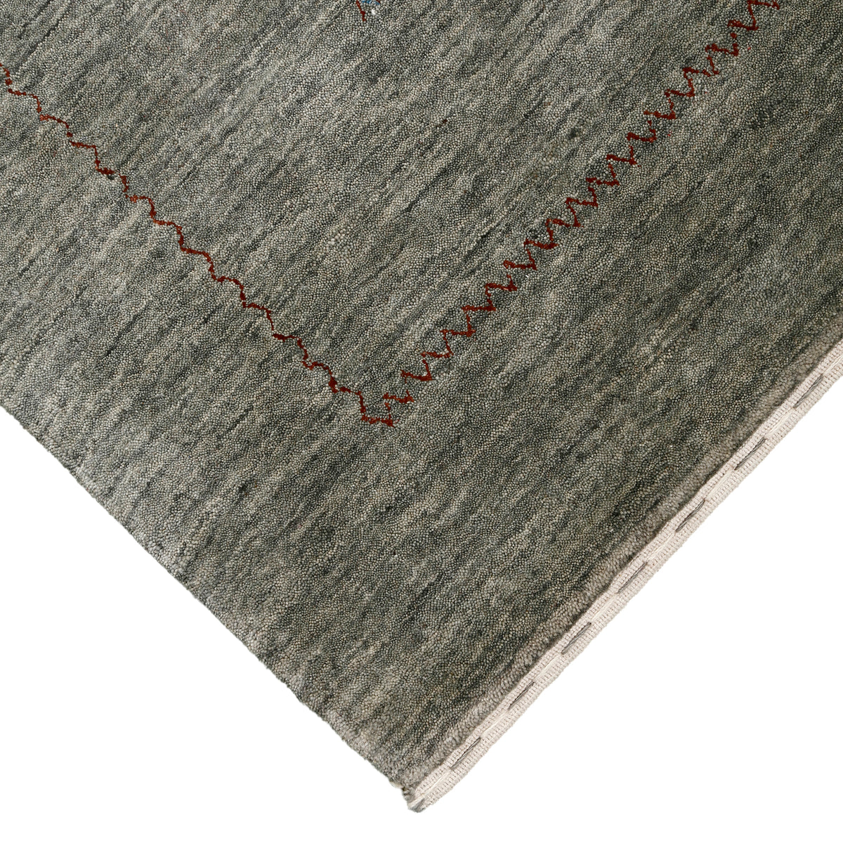 Corner and edge detail of slate grey Loom Lori wool rug showing rust-brown zigzag border and traditional handcrafted finishing