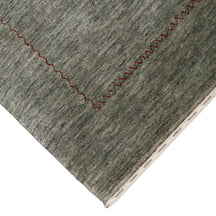 Corner and edge detail of slate grey Loom Lori wool rug showing rust-brown zigzag border and traditional handcrafted finishing