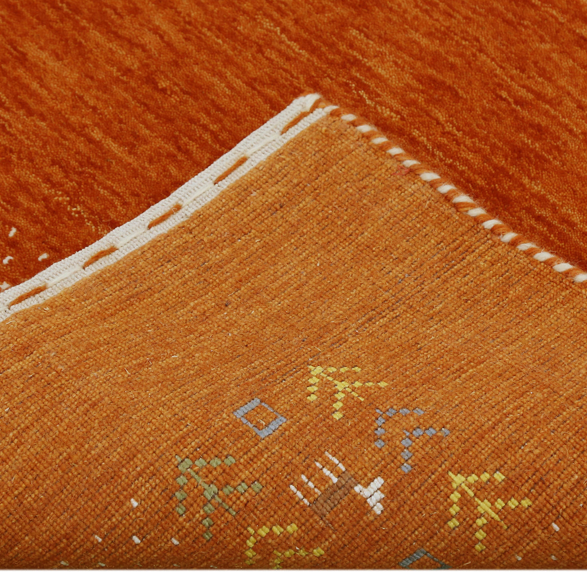 Corner and edge detail of terracotta orange Loom Lori wool rug showing ivory dotted border, tribal motifs and handcrafted finishing