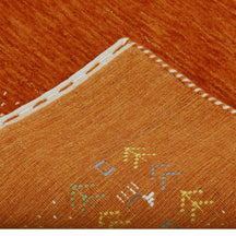 Corner and edge detail of terracotta orange Loom Lori wool rug showing ivory dotted border, tribal motifs and handcrafted finishing