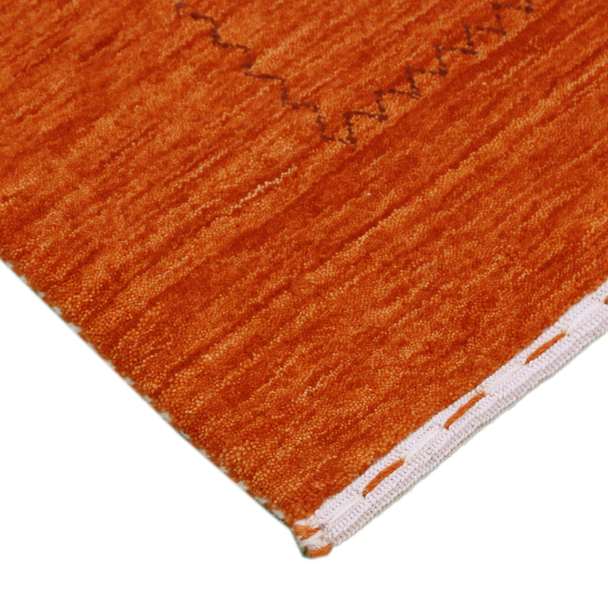 Corner and edge detail of terracotta orange Loom Lori wool rug showing subtle geometric border and handcrafted finishing