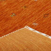 Corner and edge detail of terracotta orange Loom Lori wool rug showing subtle geometric border and handcrafted finishing