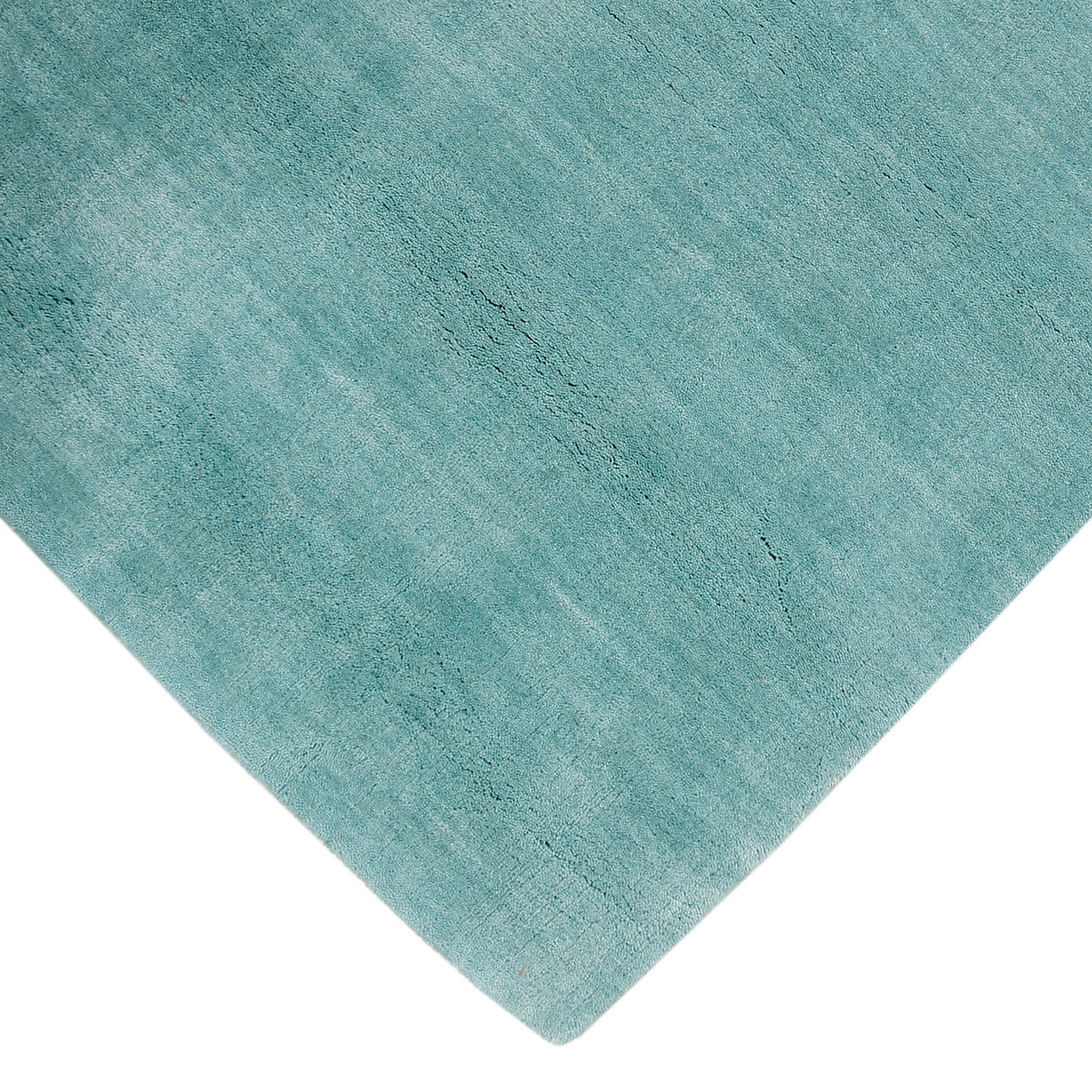 Corner and edge detail of a turquoise hand woven Loom Lori wool rug showing its neat finishing, soft surface and plush 12–15 mm pile.
