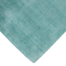 Corner and edge detail of a turquoise hand woven Loom Lori wool rug showing its neat finishing, soft surface and plush 12–15 mm pile.